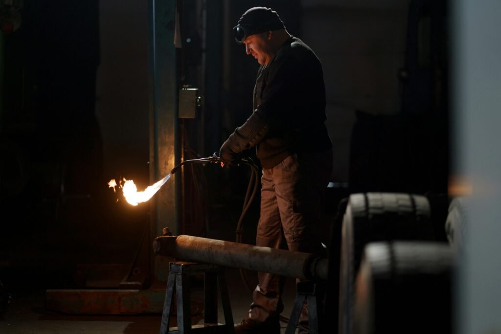 A welder skillfully operates equipment in a dimly lit industrial setting.